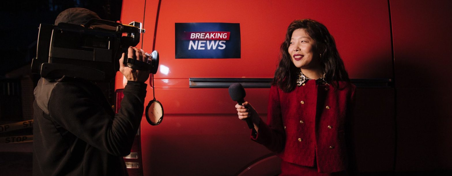 Dynamic news reporter holding microphone near red van during nighttime outdoor broadcast. — examplearticle