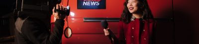 Dynamic news reporter holding microphone near red van during nighttime outdoor broadcast. — examplearticle