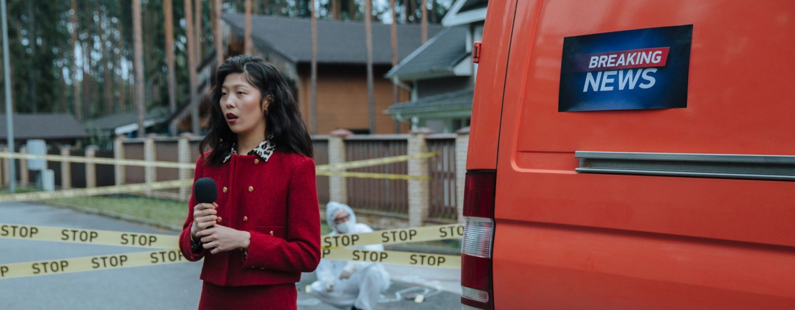 Female reporter in red outfit at an outdoor crime scene with warning tape and a news van. — LTrent Driving School: Expert Tra