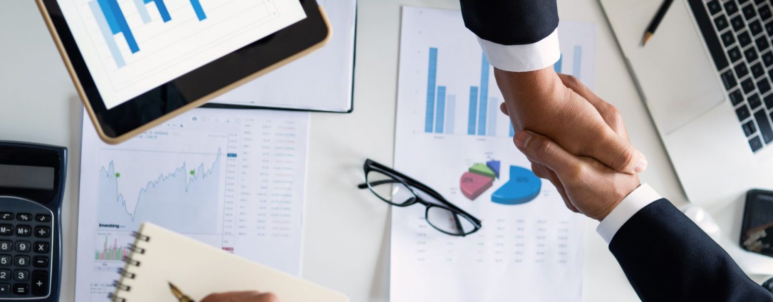 Business professionals handshake over graphs and charts in a corporate setting, symbolizing successful negotiation and agreem